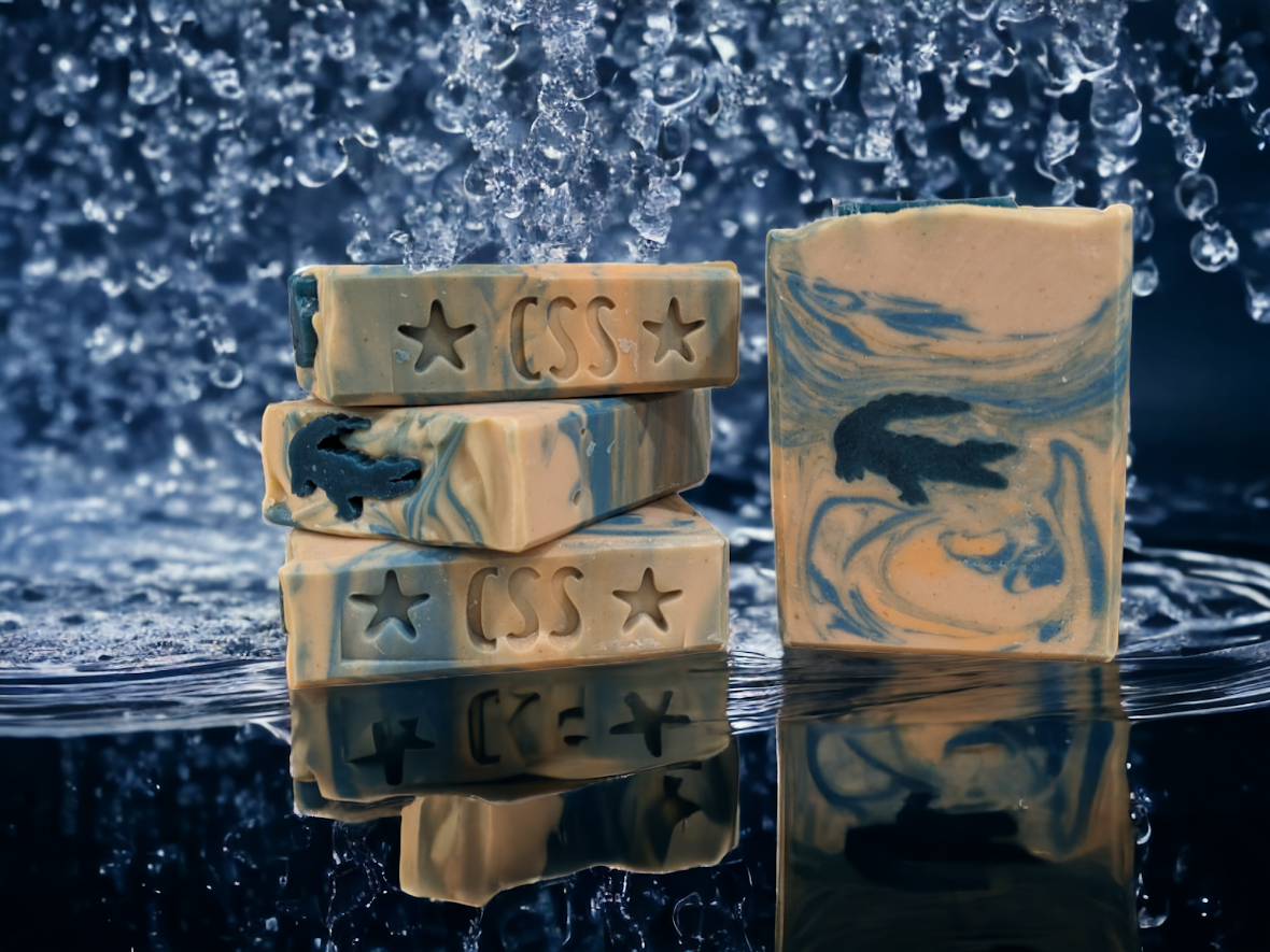 Adventure awaits with this wonderfully creamy and sudsy handcrafted tallow bar soap with alligator embeds and blue and orange swirling water. Adventure awaits with this one-of-a-kind soap! Let your imagination run wild with our Fun Alligator Tallow Soap. Handcrafted in small batches with kaolin clay, colloidal oats, soap nuts, goat's milk and a hint of Kentucky Bourbon scent that will leave you feelin' refreshed all day.