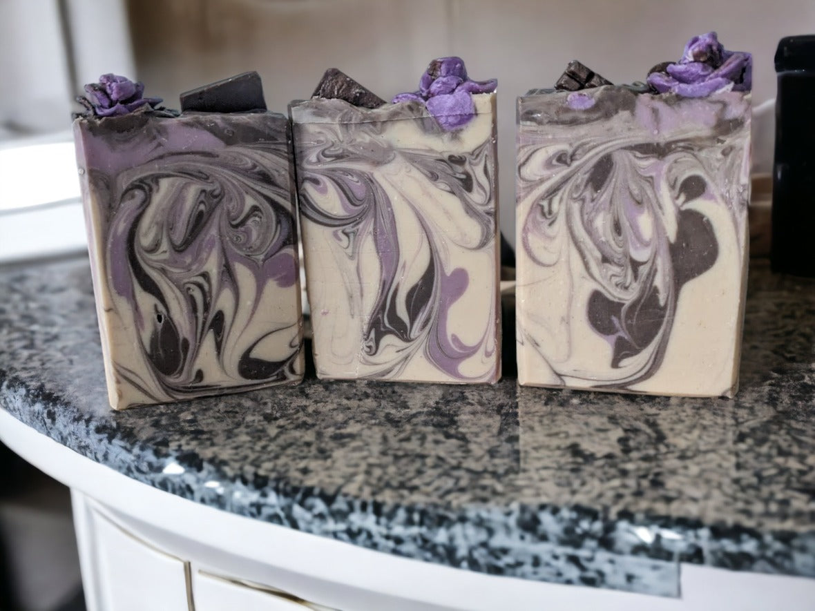 Up your shower and bath game with this small batch chocolate-lavender butter soap bar! Handcrafted design elements that include divine whispy swirls in chocoloate brown and lavender, and topped with chocolate lavender soap roses, your skin will feel as smooth as the butters it's created with.  Scented with a divine chocolate and lavender fragrance!  This delectable, skin lovin’ butter bar is a must buy, must try!