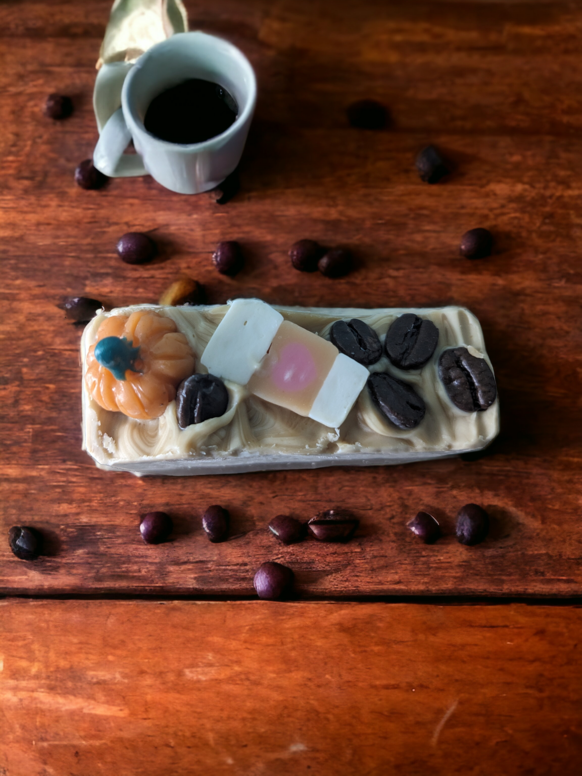 Luxury Artisan Bar soap – Pumpkin Spice Latte To Go.  The top of the handcrafted soap bar has a creamy white top that is decorated with delightful pumpkins, a to go coffee cup and coffee beans.  The body of  the bar of soap has light latte brown with a pumkpin and to go coffee cup that go through the width of the soap.