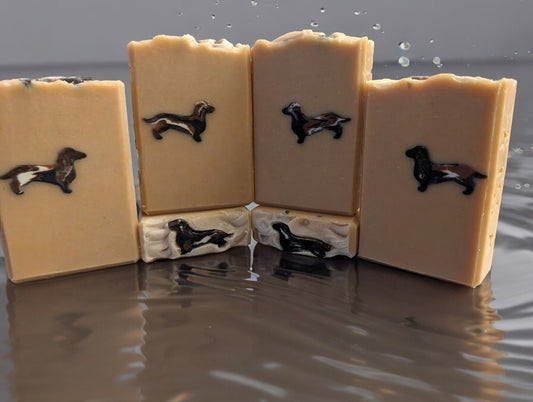 Beige colored soap bar featuring a dapple dachshund dog soap embed.  Handcrafted with skin loving ingredients like Kaolin Clay, Colloidal Oats and Goat Milk, this is the perfect addition to your skin care routine or a perfect gift for the doxie lover in your life.