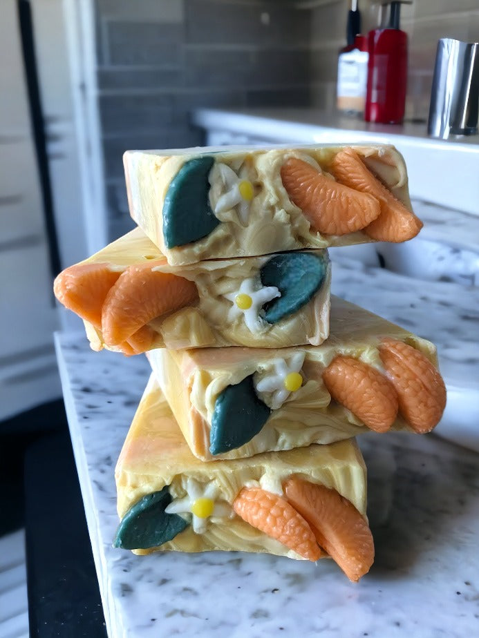 Take a dreamy shower with Tangerine Dream Soap! This soap is topped with tangerine wedges, a small white tree bud and leaf.  The body of the soap has 3 layers:  bottom and middle:  solid tangerine and white layers and the top layer has swirls of white, tangerine and yellow.  This burst of tangerine goodness will leave you feeling refreshed and revitalized. Our unique blend of luxury oils and butters is sure to make you "peel" good!