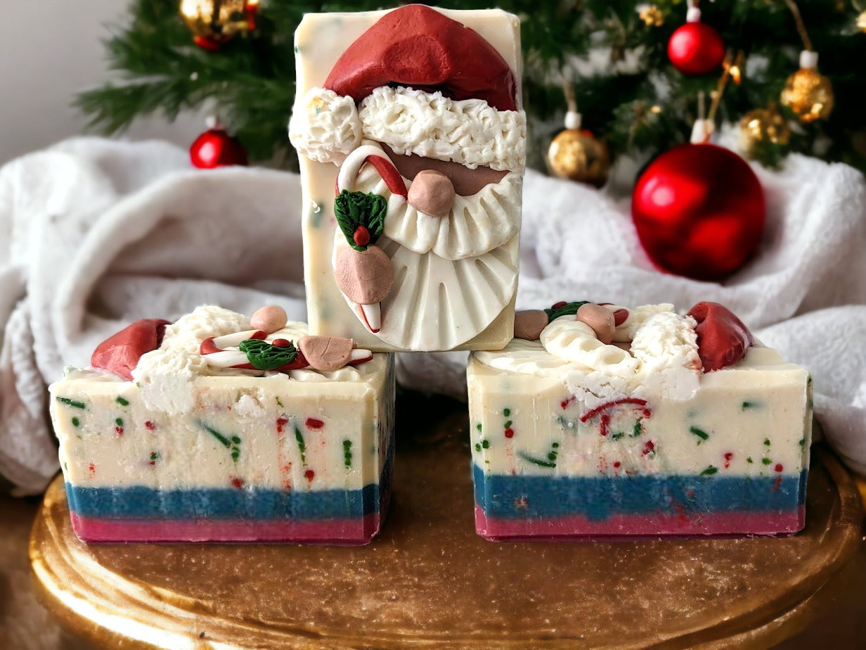 Handmade bar Soap with a Santa Claus head on top.  Santa is holding a candy cane.  Body of the soap is layered starting with red, then green and a creamy white with red and green soap sprinkles.