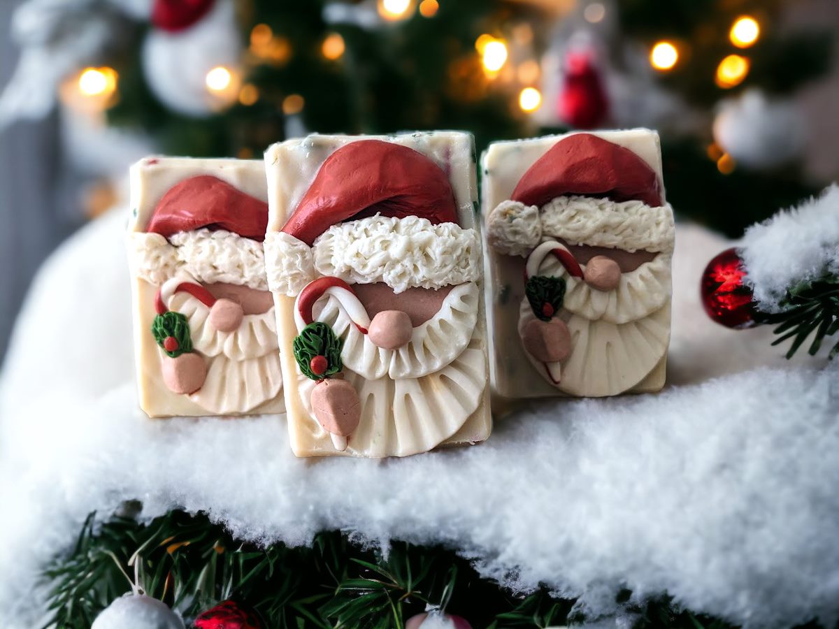 Handcrafted bar Soap with a Santa Claus head on top.  Santa is holding a candy cane.  Body of the soap is layered starting with red, then green and a creamy white with red and green soap sprinkles.