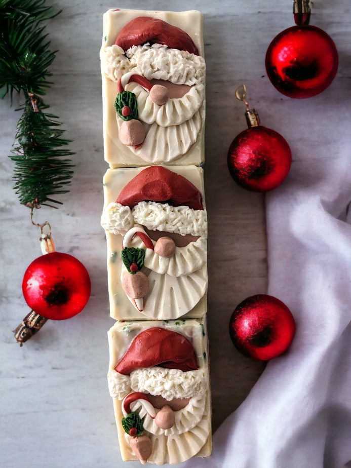 Handcrafted bar Soap with a Santa Claus head on top.  Santa is holding a candy cane.  Body of the soap is layered starting with red, then green and a creamy white with red and green soap sprinkles.