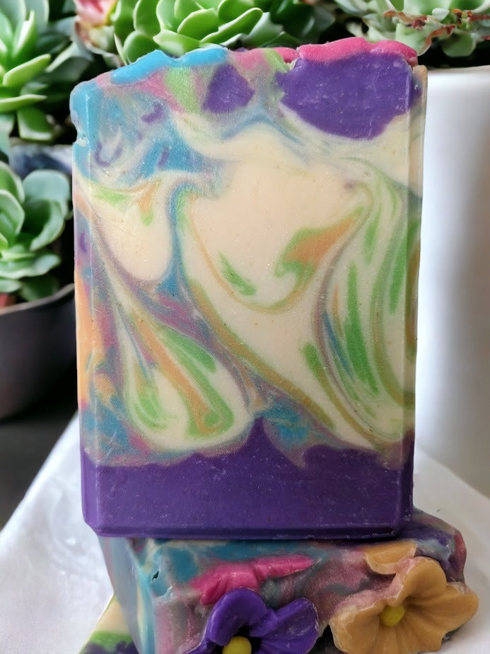 Delightful, decorative spring soap scented with midnight peonies.  Handcrafted Soap flowers in spring colors adorn the top of this luxury soap bar! Gentle swirls throughout the soap in the same color as the flowers in purple, pink orange, green and caribbean blue. Handmade in small batches with skin-loving Shea, Mango, Cocoa and Kokum butters.