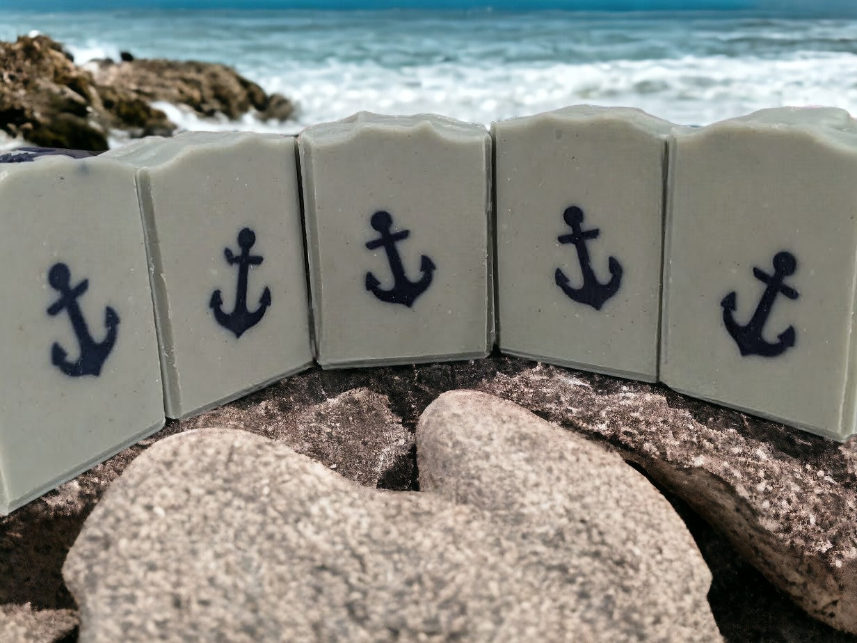 Simple, handcrafted goat milk soap featuring a navy blue anchor against a greenish-blue background. Scented with 'Salty Mariner' the scent is a blend of a blend of lily of the valley, jasmine, leafy greens, pine, and musk, with a splash of fresh rain.