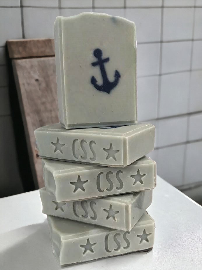 Simple, great for your skin tallow and goat milk soap featuring a navy blue anchor against a greenish-blue background. Scented with 'Salty Mariner' the scent is a blend of a blend of lily of the valley, jasmine, leafy greens, pine, and musk, with a splash of fresh rain.